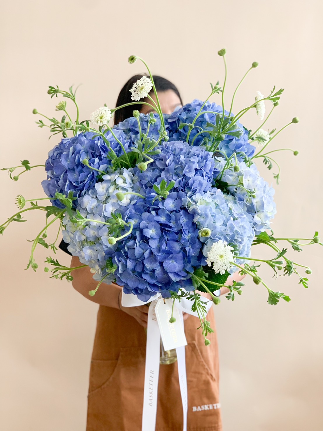 stunning bouquet featuring a mix of pastel-colored hydrangeas in shades of blue and white, complemented by delicate green foliage and wrapped in soft paper