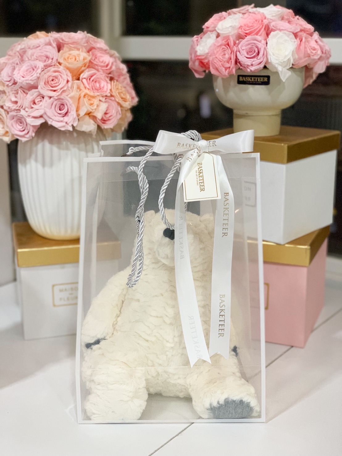 Soft white plush teddy bear inside a transparent gift bag with a Basketeer satin ribbon, perfect for gifting.