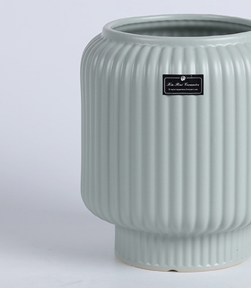 Close-up of a light green ribbed ceramic vase with elevated base.