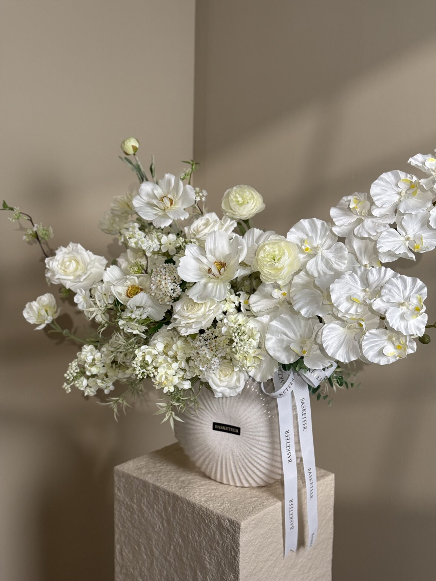Modern white floral arrangement in ceramic vase with orchids, roses, and mixed white blooms.