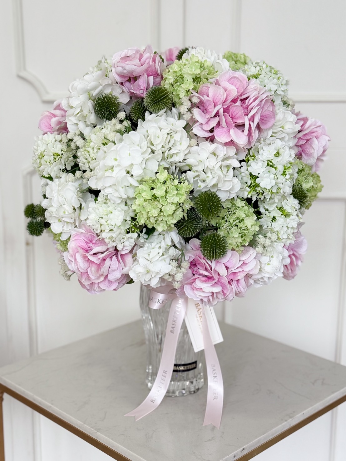 Luxury glass vase with pastel hydrangeas in white, green, and pink tones, accented with greenery.