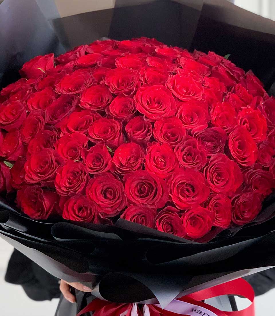 close-up view of a vibrant mixed bouquet featuring color full roses, orange ranunculus, white flowers, and green foliage, tied with a pink ribbon.