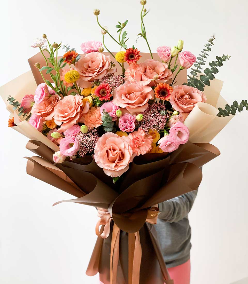 stunning bouquet of mixed pastel flowers, including white roses, pink roses, and white lilies, elegantly wrapped in a paper wrap.