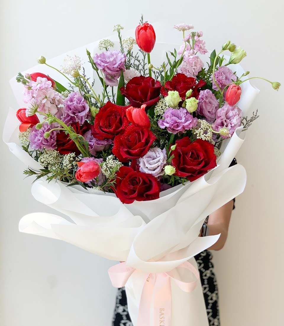 beautiful bouquet featuring vibrant red roses and purple flowers, elegantly wrapped in white paper with a light pink ribbon.