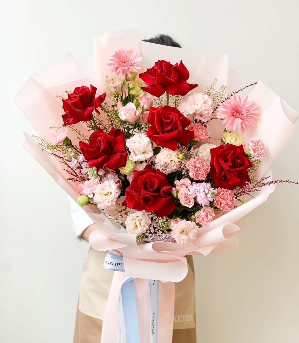 Stunning bouquet of red roses and soft pink carnations, complemented by delicate baby's breath and lush greenery, wrapped in pink paper and finished with a light blue ribbon.