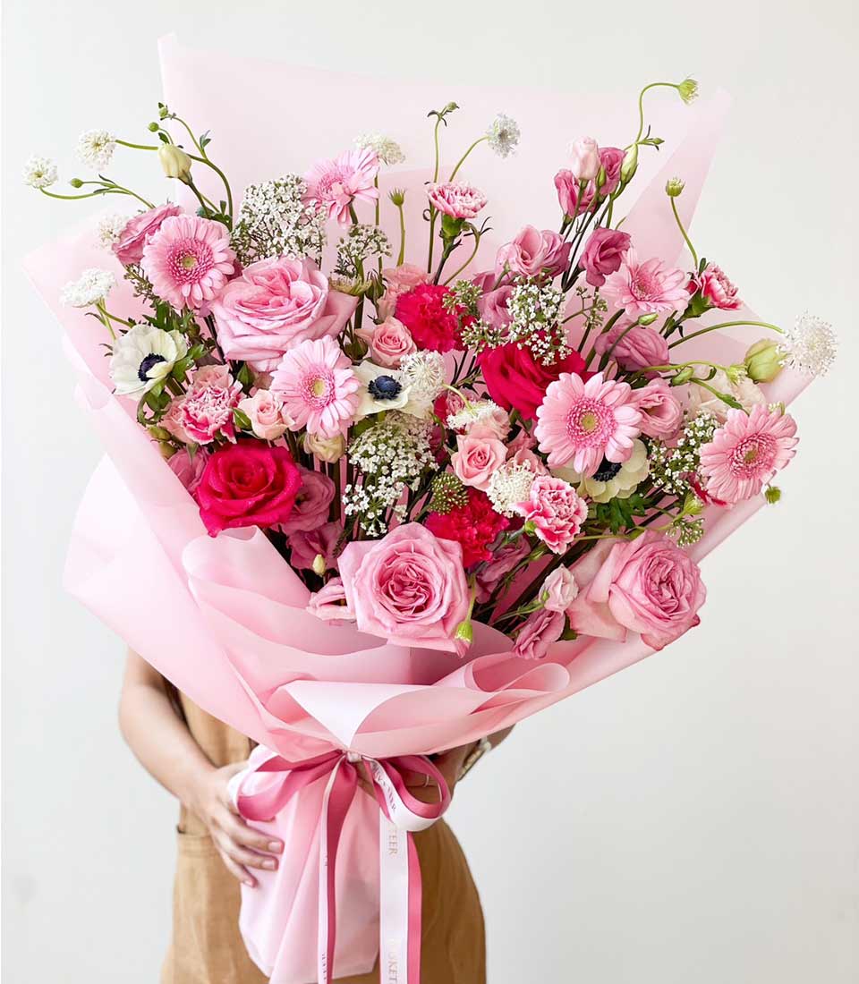 stunning bouquet of pink flowers featuring pink roses, gerbera daisies, and other seasonal blooms, elegantly wrapped in pink paper and tied with a matching ribbon