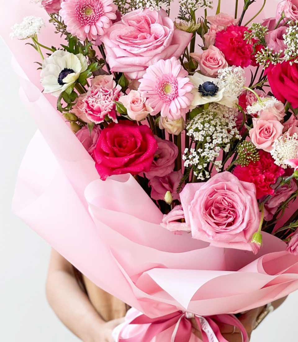Elegant bouquet of mixed pink and white flowers, featuring roses, gerbera daisies, carnations, and filler flowers, wrapped in pink paper and tied with a pink ribbon