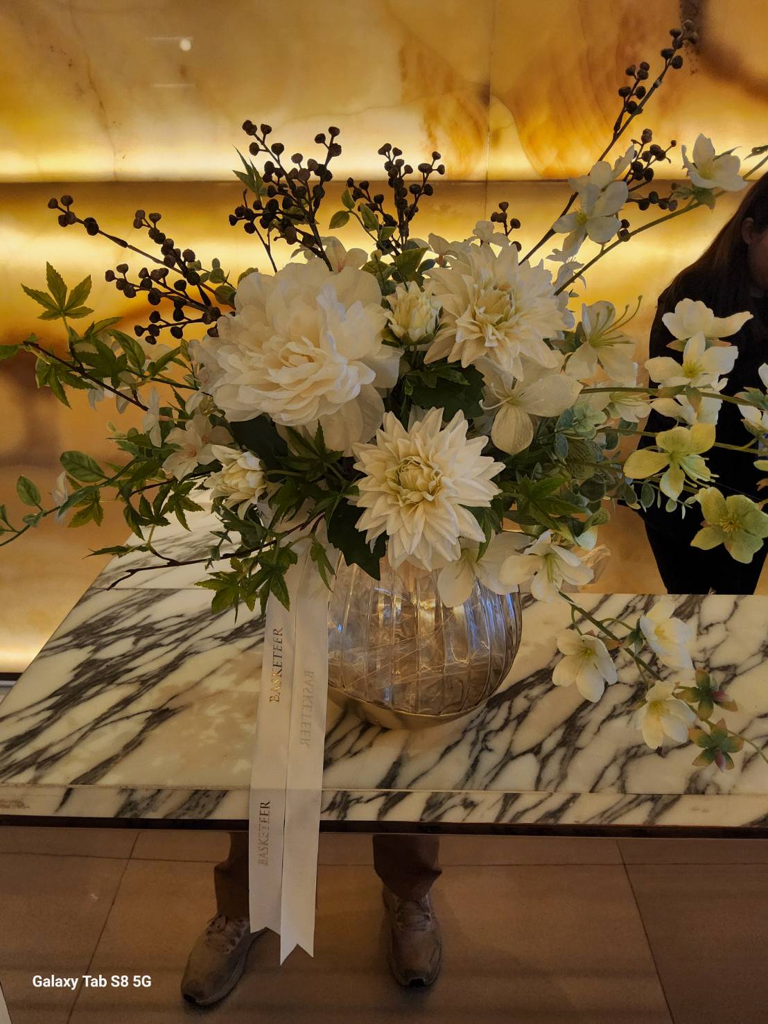 A stunning white artificial floral arrangement with lifelike dahlias and delicate blossoms in a modern glass vase, perfect for elegant home and office decor.