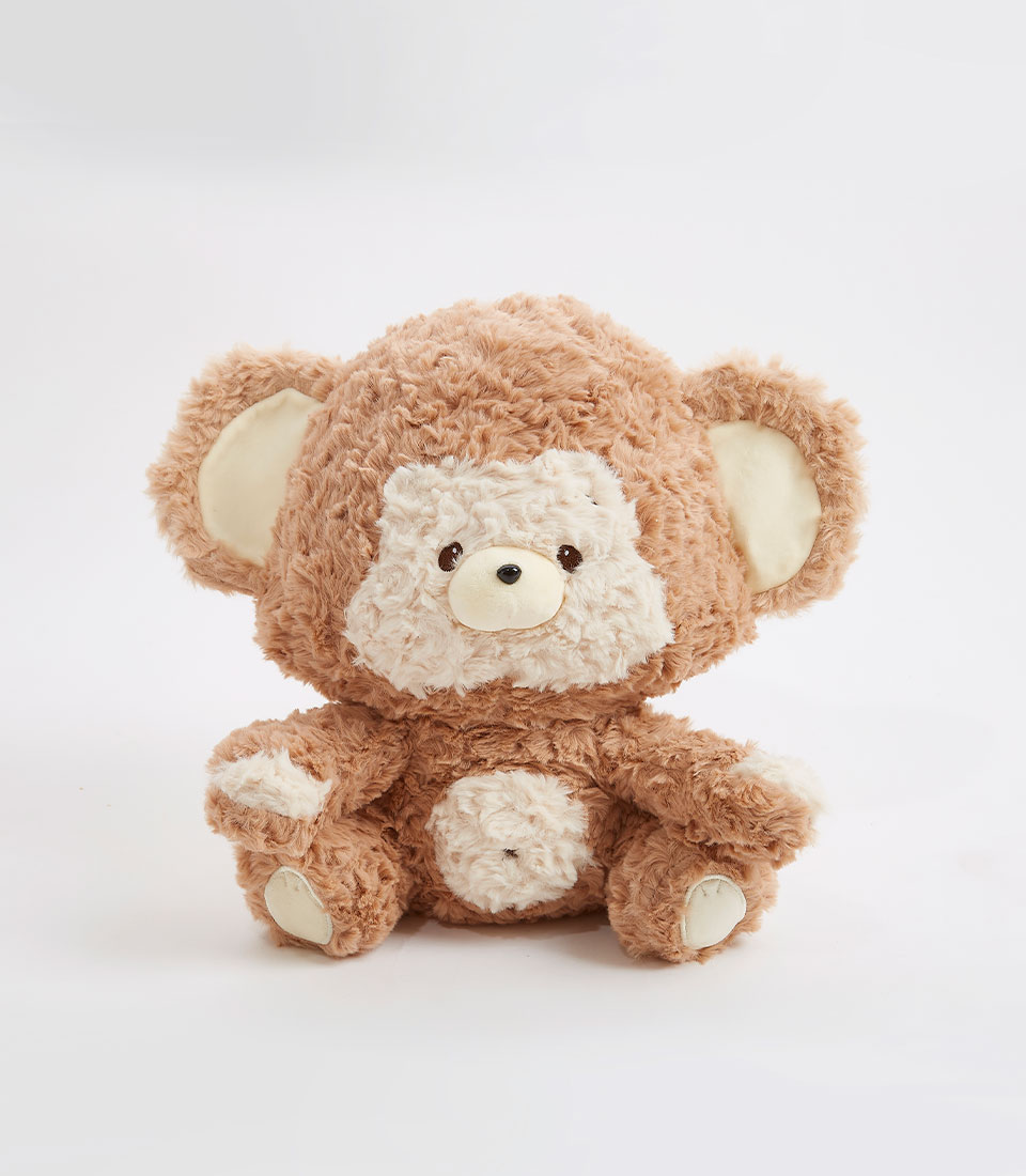 An adorable brown teddy bear soft toy with light brown fur and a contrasting beige snout, belly, and inner ears is sitting against a plain white background. The bear has round, dark eyes and a small brown nose. Its limbs and ears are slightly oversized, giving it a cute and cuddly appearance.