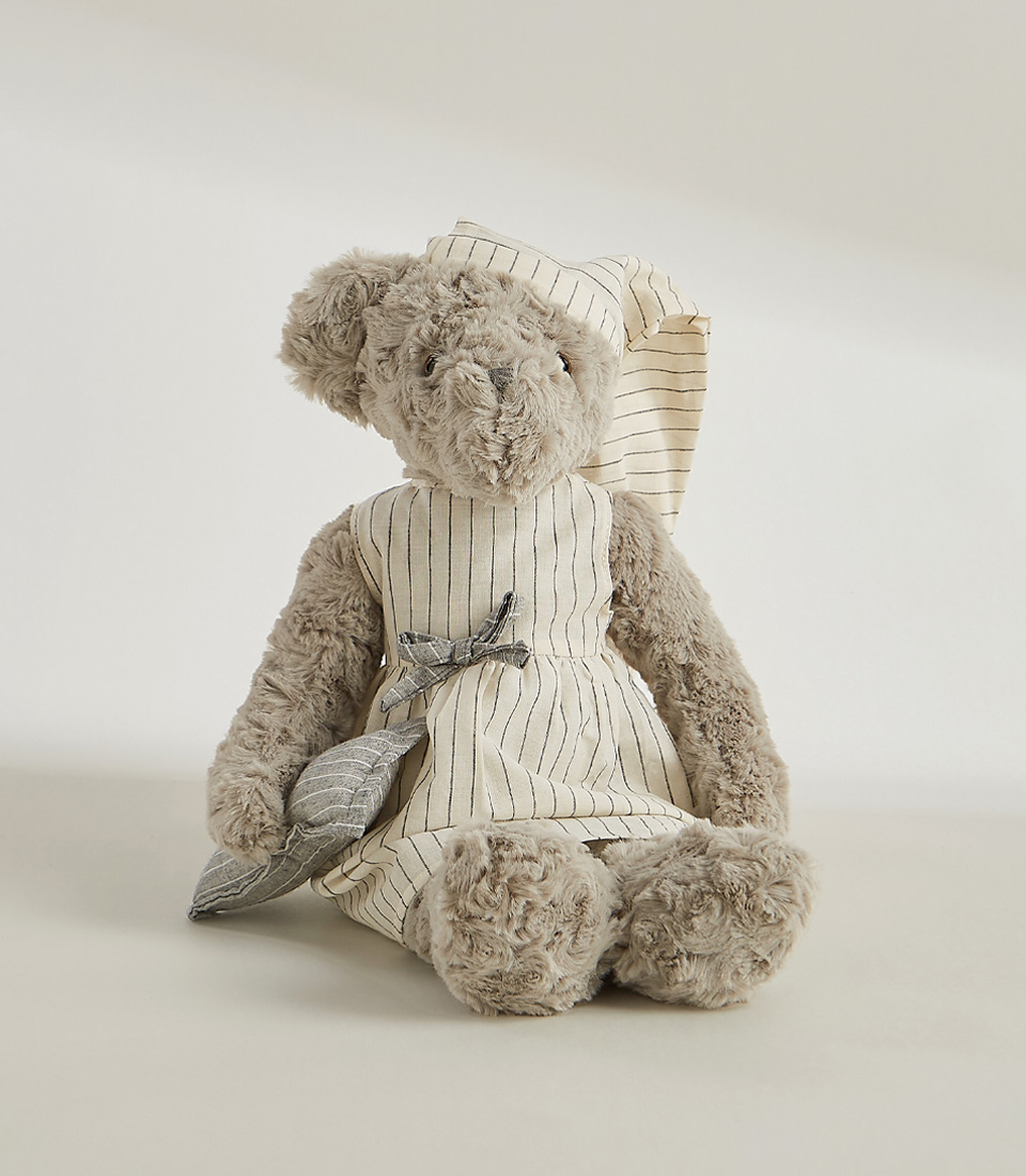 A grey teddy bear wearing a striped nightgown and matching nightcap, standing and ready for bedtime, set against a light gray background.