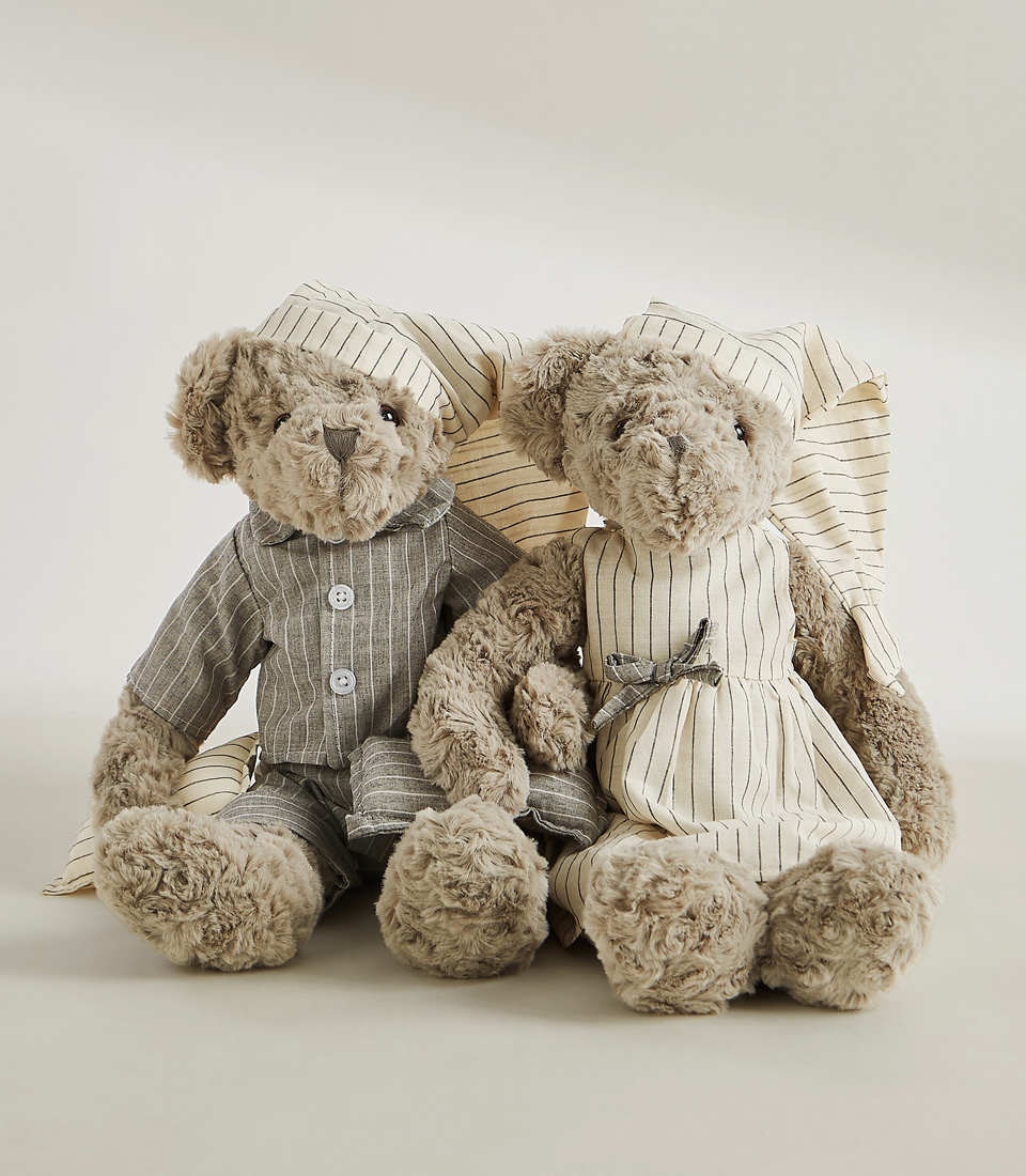 A set of two grey teddy bears dressed in matching striped pajamas and nightgowns, complete with nightcaps, set against a light gray background.