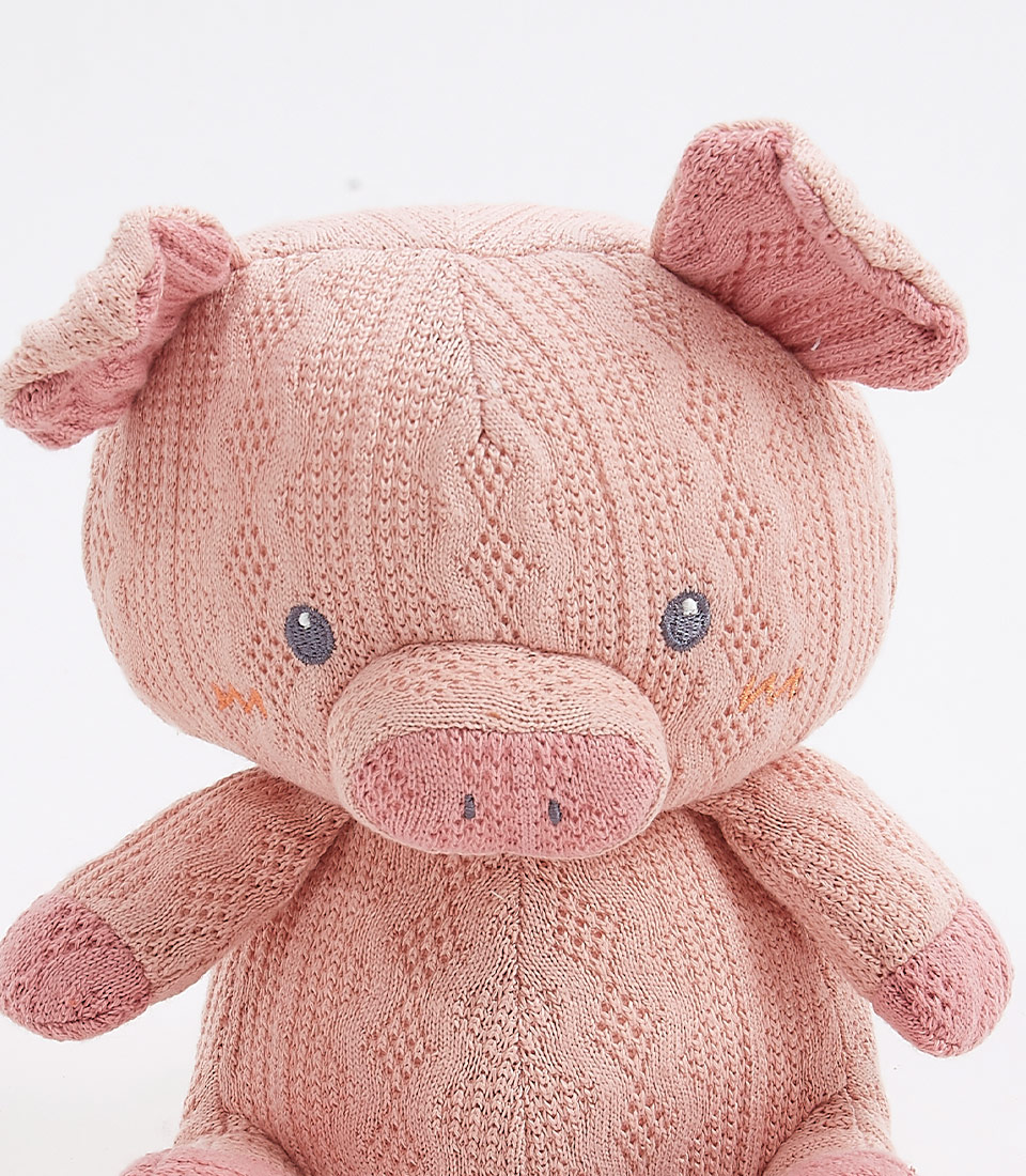 Close-up view of a handcrafted crocheted pig plush toy, with a soft pink exterior. The toy features a friendly design with embroidered eyes and a cute snout, perfect for newborns and young children.