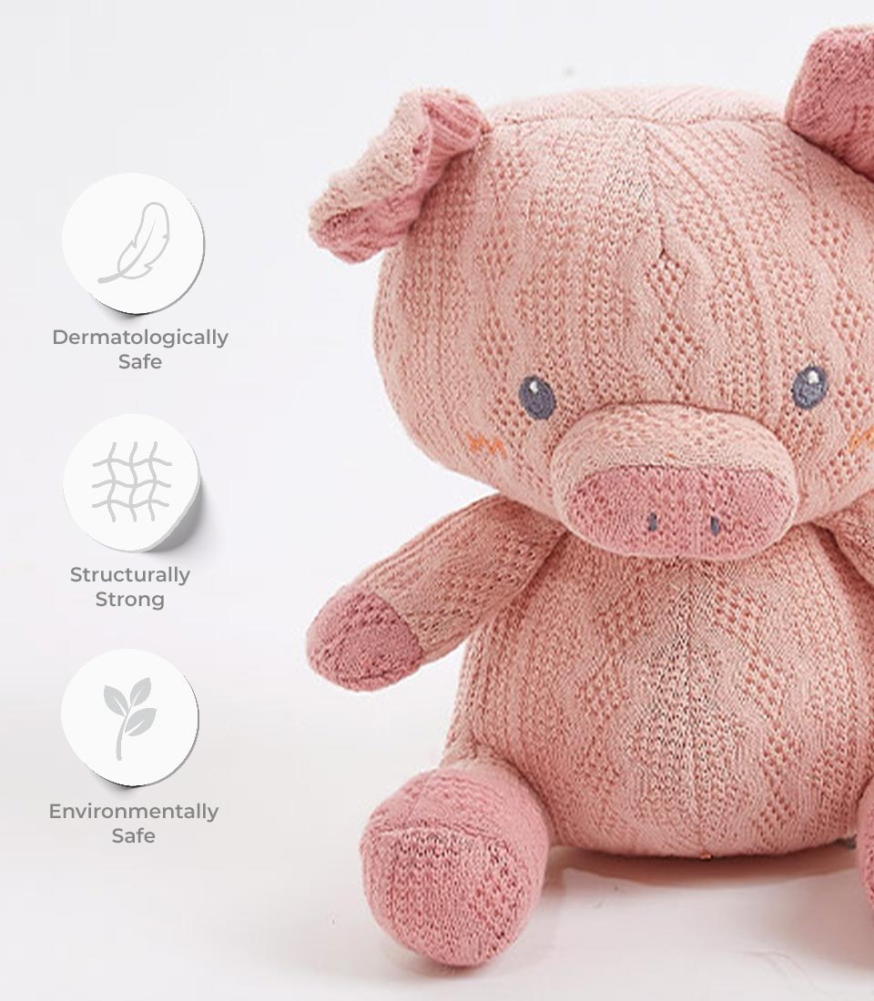 Close-up of a pink crocheted pig plush toy, showcasing its dermatologically safe, structurally strong, and environmentally safe features. The toy has embroidered eyes, a soft texture, and is designed for newborns and young children.
