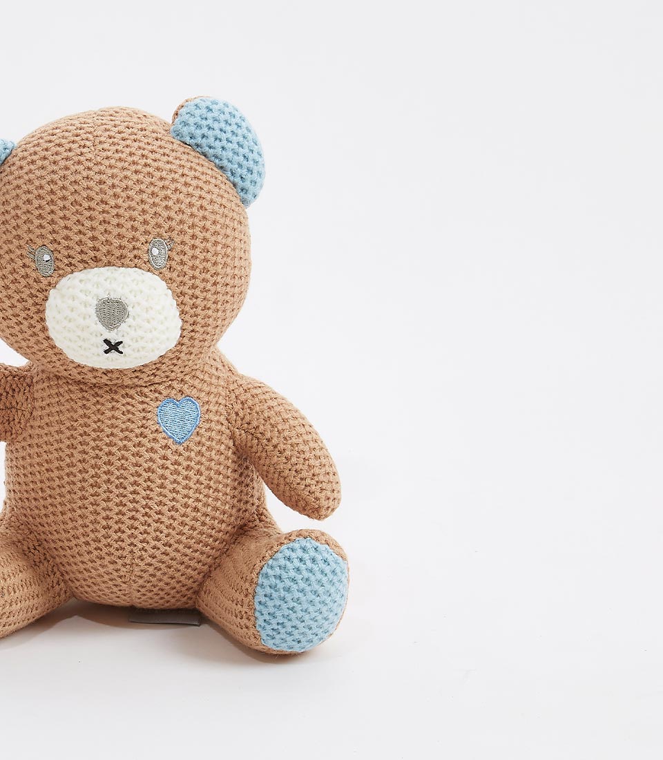 Close-up of a cute brown crocheted teddy bear with blue accents on its ears, paws, and a heart detail on its chest. Designed for newborns and young children.