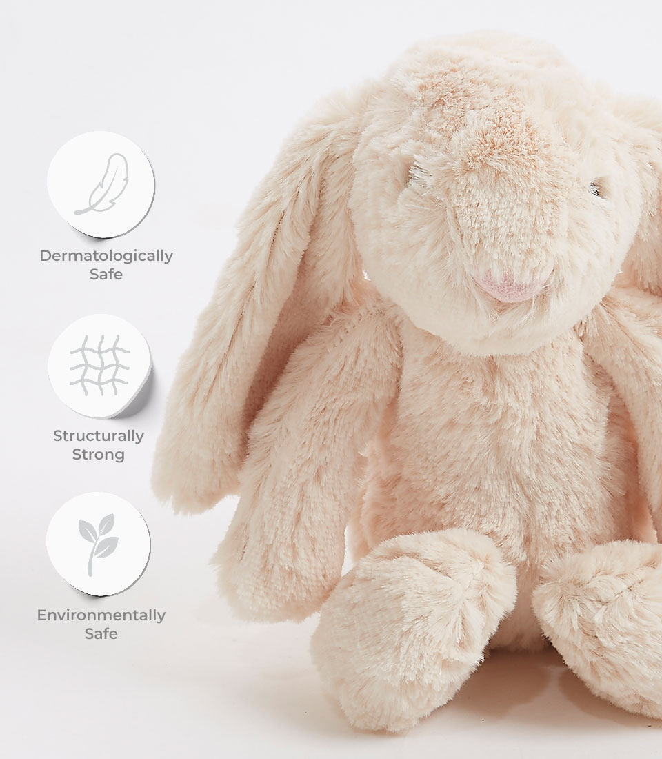 Close-up of a soft beige plush bunny toy with long floppy ears and an embroidered face, labeled as dermatologically safe, structurally strong, and environmentally safe.