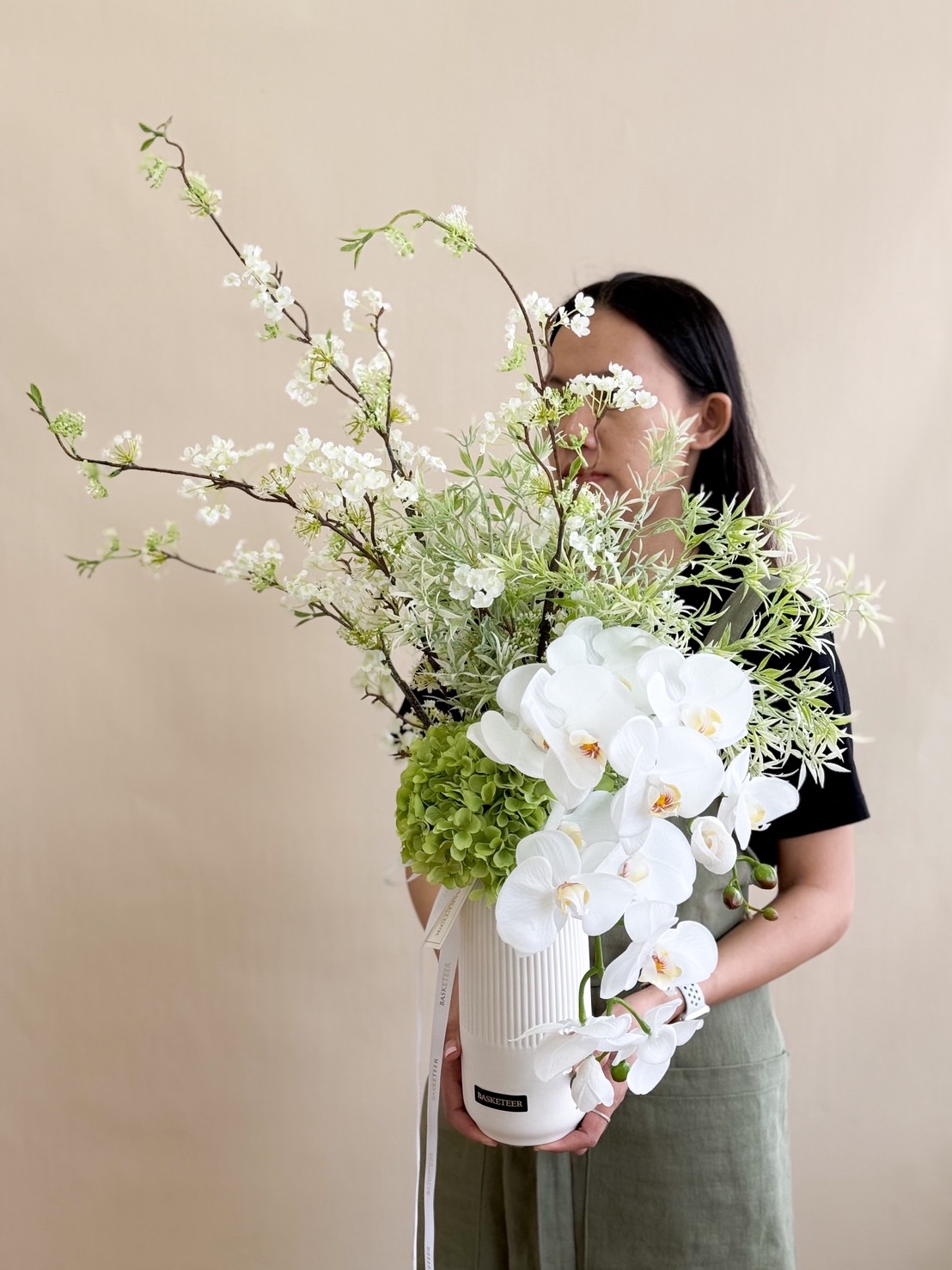 Tall white vase with cascading white phalaenopsis orchids, green hydrangeas, and airy white filler branches