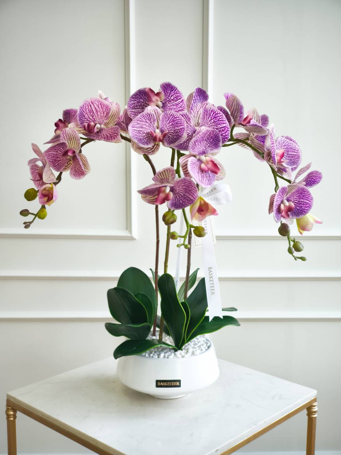 Elegant purple phalaenopsis orchids in a white ceramic pot with decorative stones – luxury orchid plant for home or office