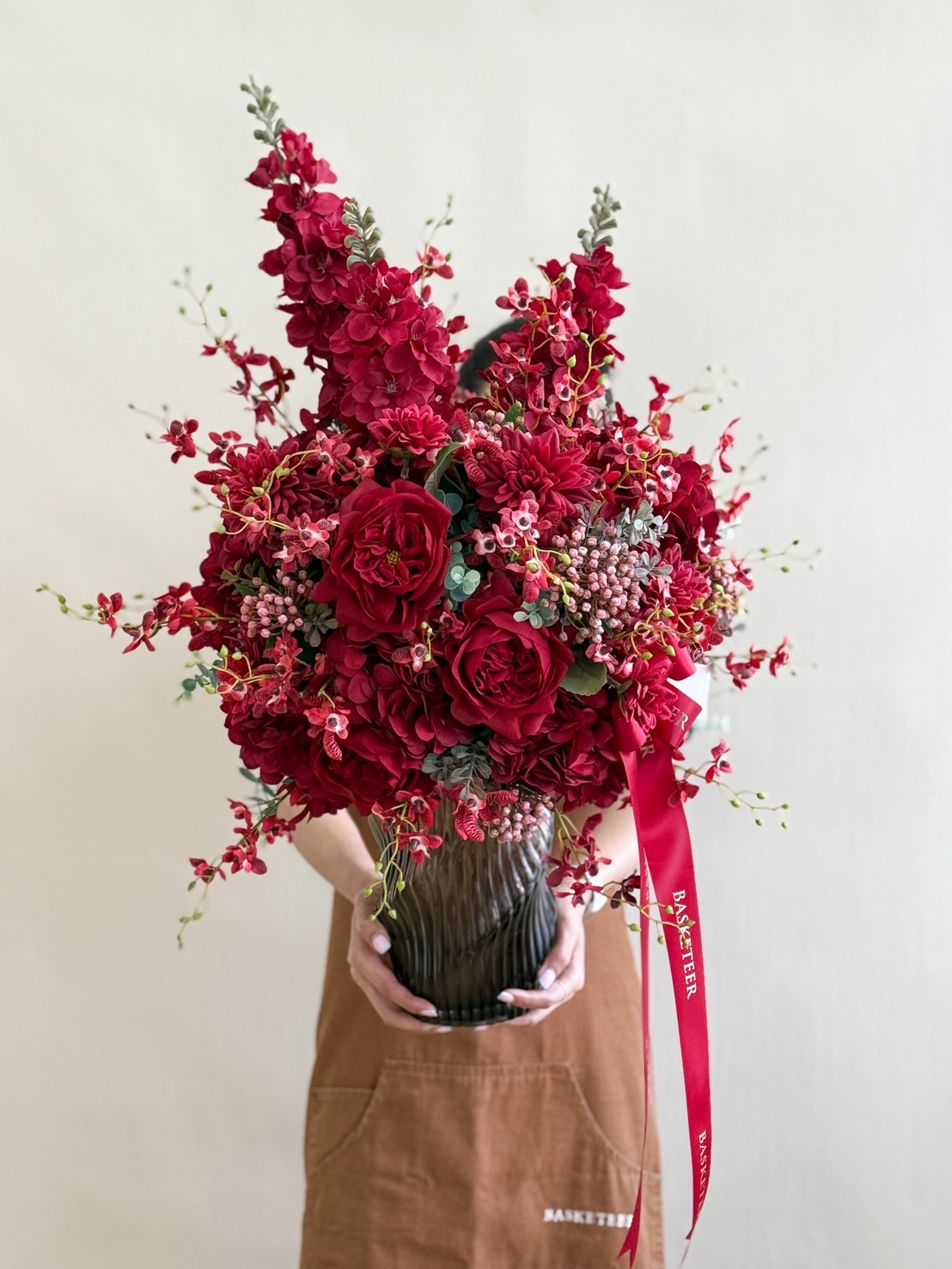 Elegant flower arrangement with red roses, orchids, and mixed red blooms in a tall fluted glass vase – luxury floral gift.