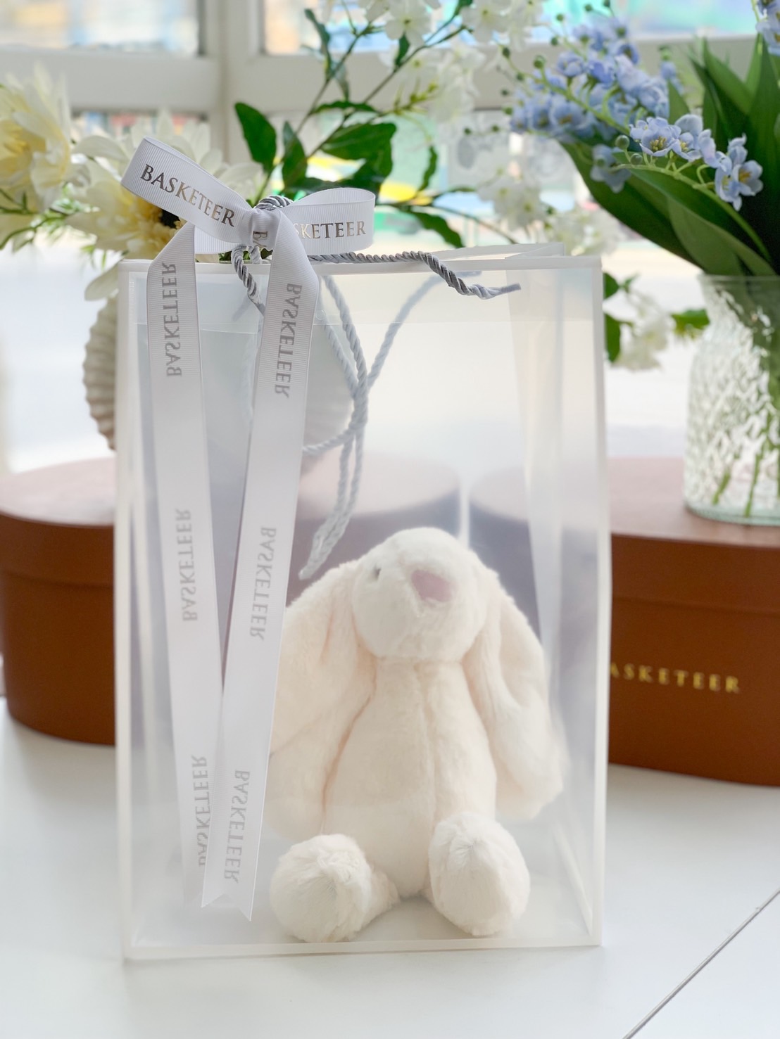 Cream plush bunny toy inside a luxury translucent gift bag with white Basketeer ribbon.