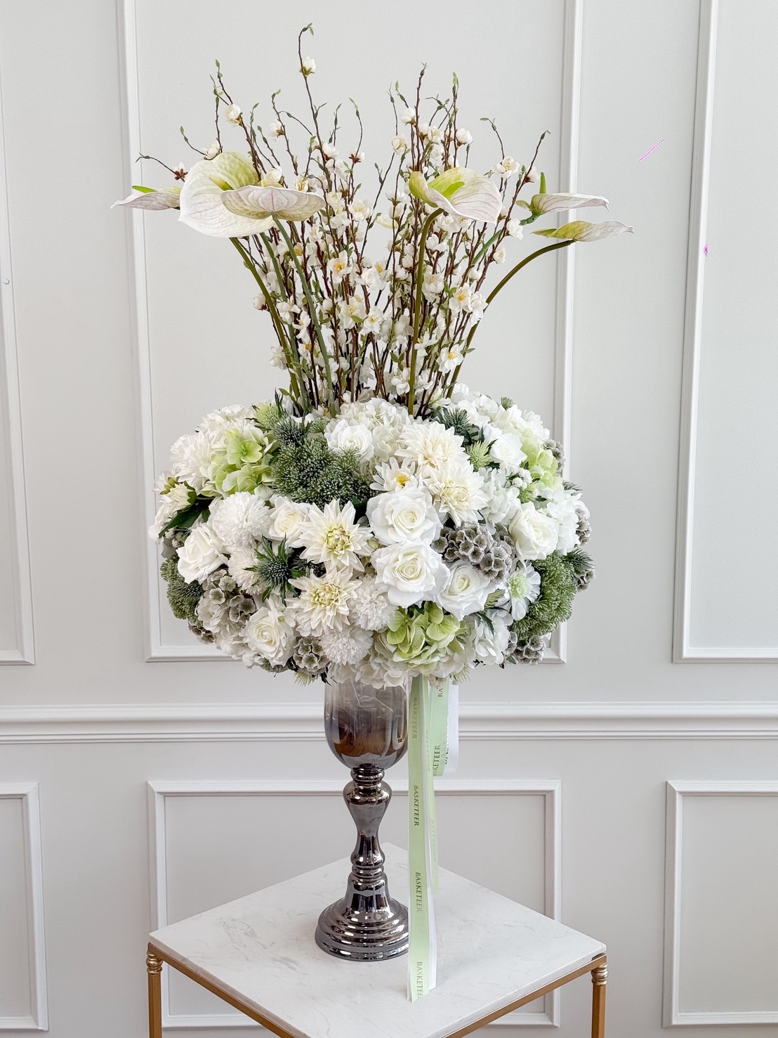 Luxury white-green flower vase with anthuriums, roses, hydrangeas, and flowering branches in a tall silver pedestal glass.