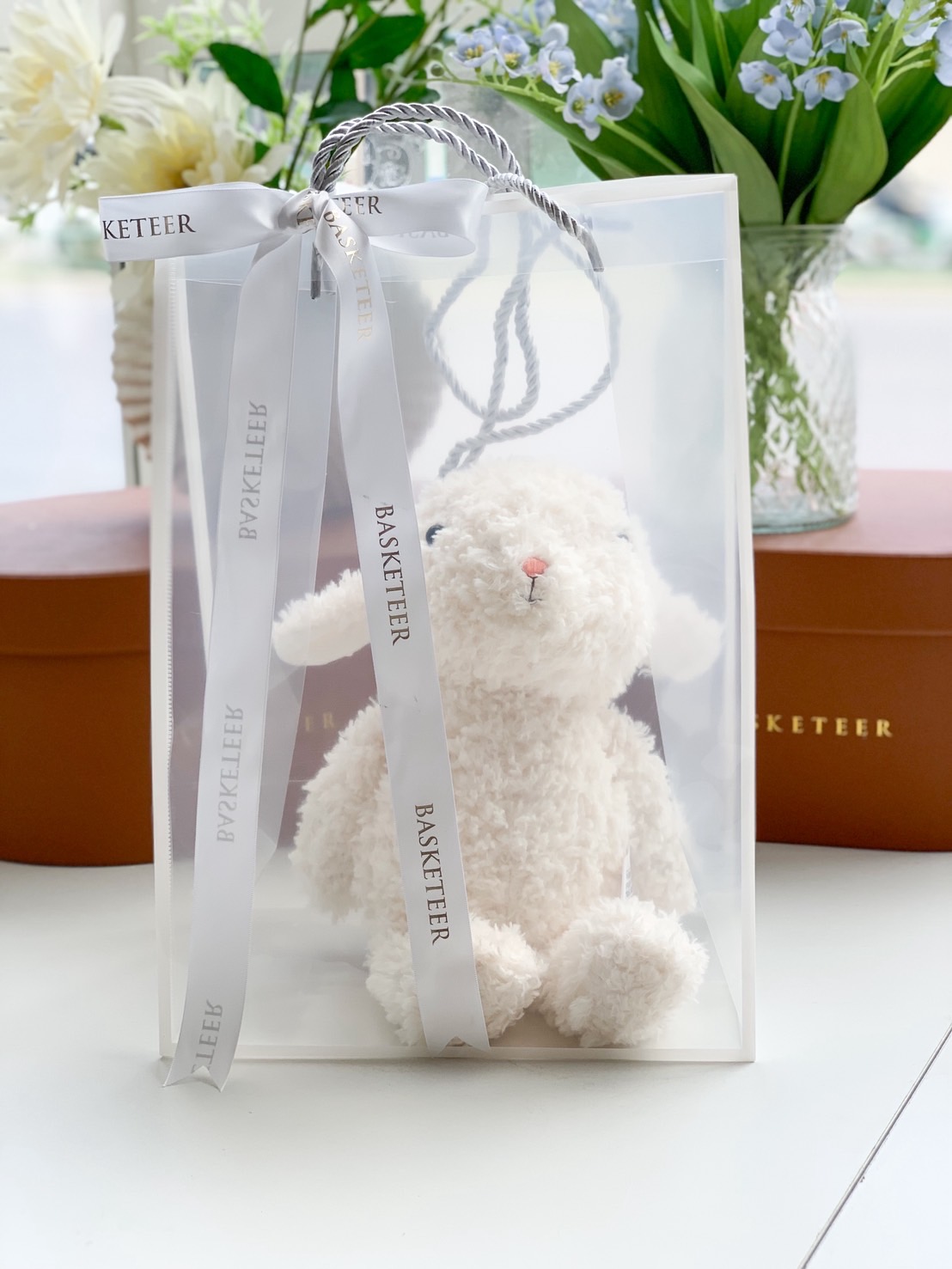 White fluffy lamb plush toy in a clear luxury gift bag with white satin ribbons.