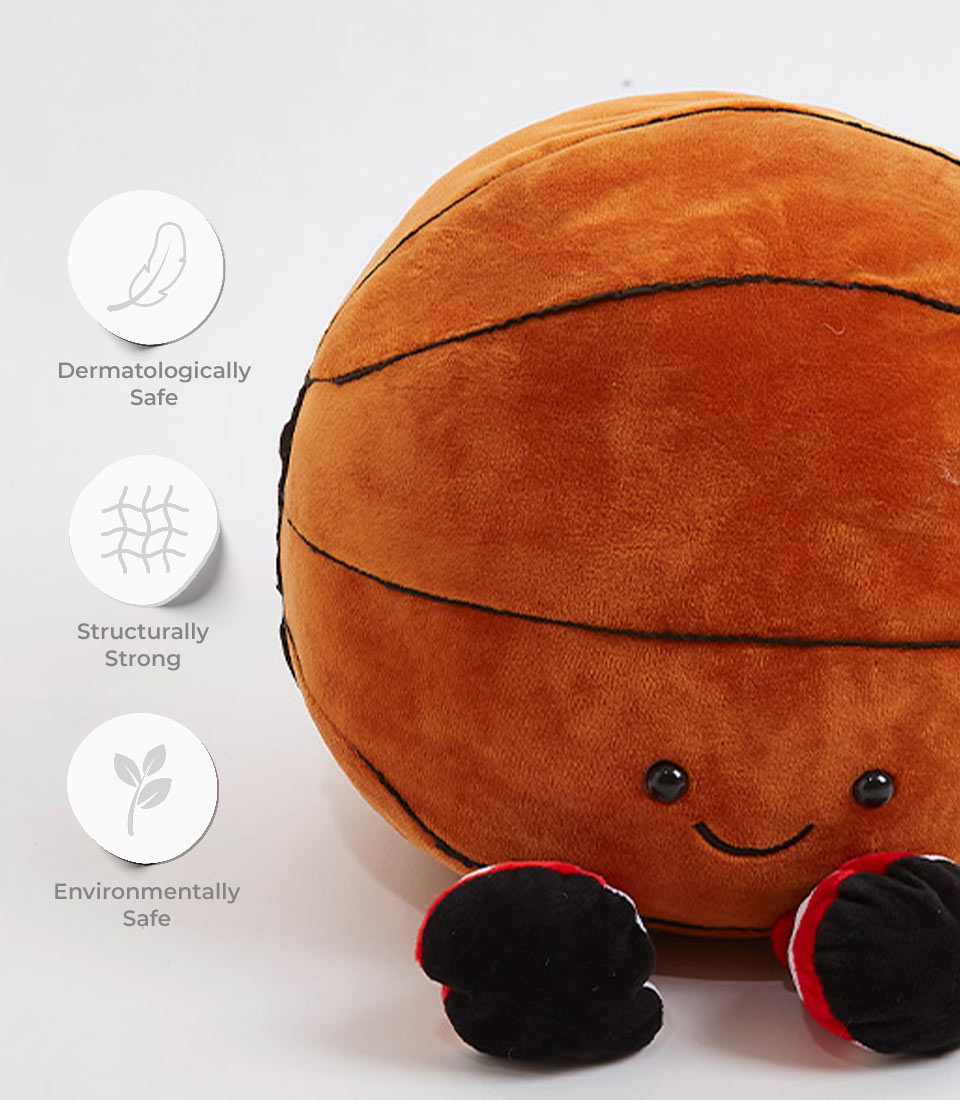A plush toy resembling a cute basketball with a smiling face, black button eyes, and small limbs wearing red and black shoes. Adjacent icons highlight features: dermatologically safe, structurally strong, and environmentally safe.