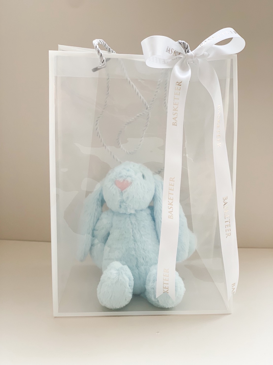 Soft blue stuffed bunny with floppy ears in a premium transparent gift bag with white ribbon.