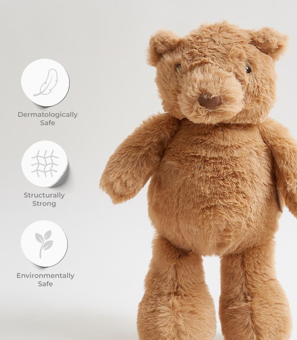 A plush teddy bear with light brown fur is shown against a plain background. Icons with accompanying text highlight the bear's features: dermatologically safe, structurally strong, and environmentally safe.