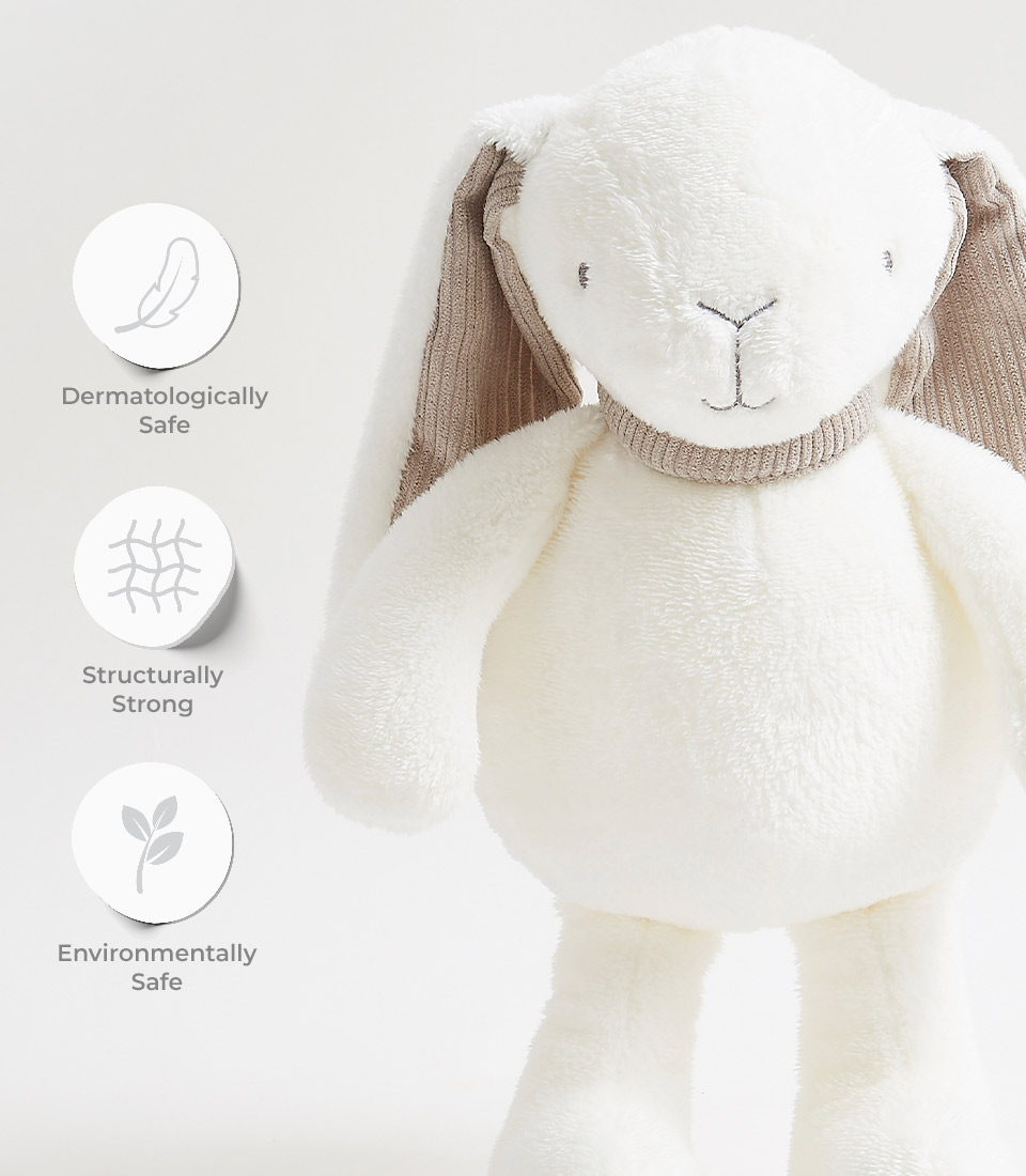 A white stuffed bunny with brown, ribbed ears and a knitted neck detail is shown against a white background. Icons to the left indicate the bunny is dermatologically safe, structurally strong, and environmentally safe.