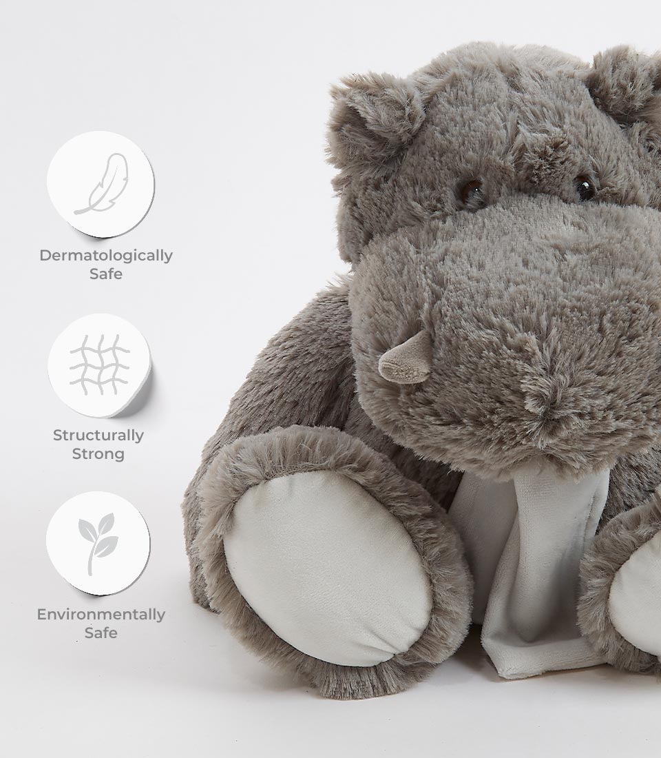 A cuddly, grey hippopotamus toy stands against a white background. Icons indicate it's dermatologically safe, structurally strong, and environmentally friendly, featuring a feather, a grid pattern, and a leaf respectively.