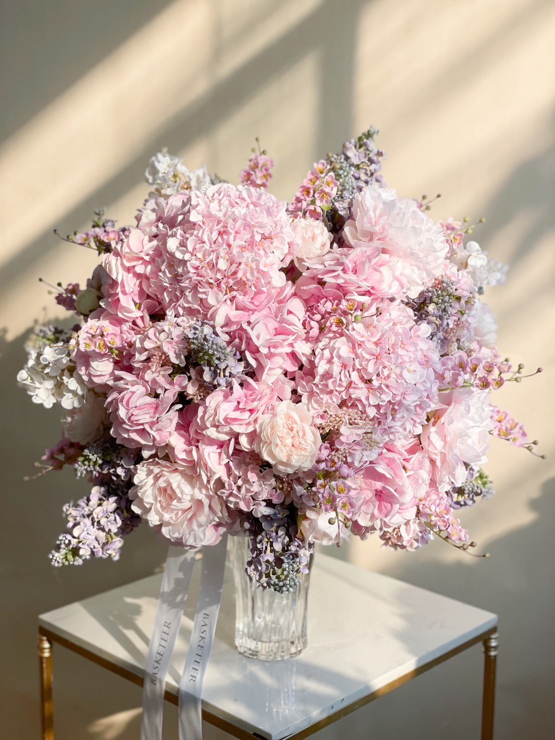 A luxurious bouquet of pink hydrangeas and peonies in a glass vase, beautifully arranged with pastel florals.