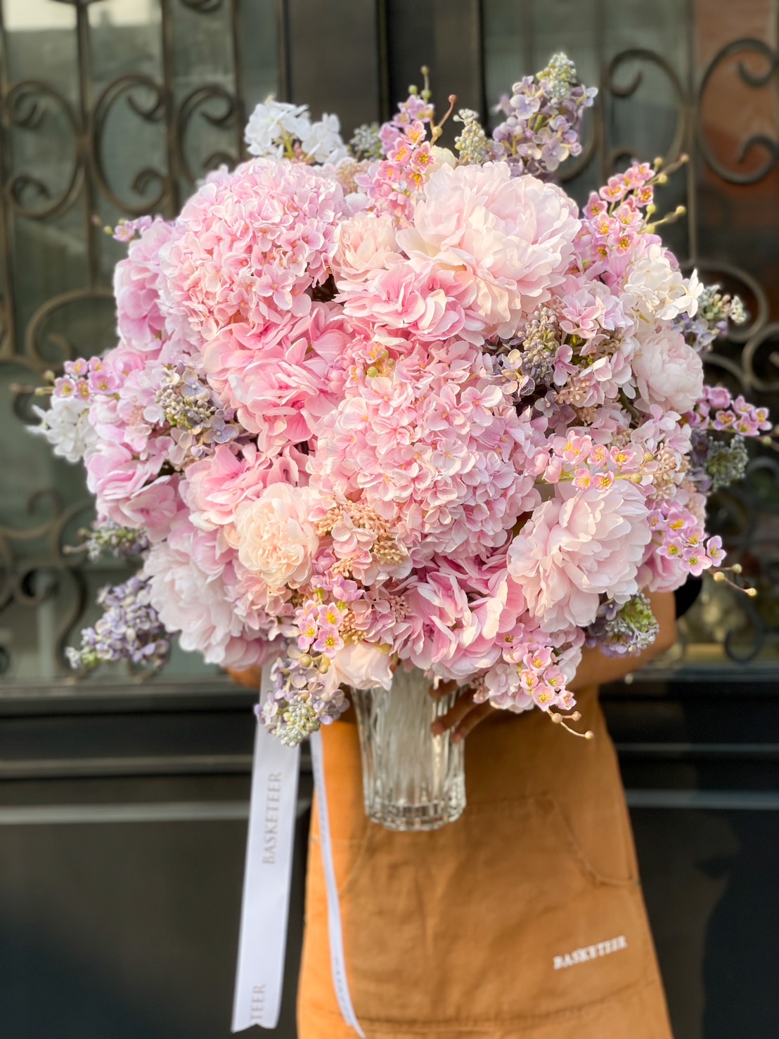 A luxurious bouquet of blush pink hydrangeas, peonies, and delicate blooms in a glass vase, elegantly wrapped with a ribbon.