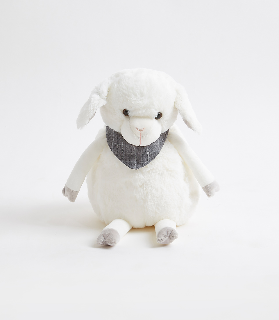 A plush white lamb toy, part of the Fluffy Sheep Soft Toys collection, is seated against a plain white background. The lamb has floppy ears, a round body, and is wearing a small dark grey patterned bib. Its feet and the inside of its ears are light grey. The toy appears soft and cuddly.