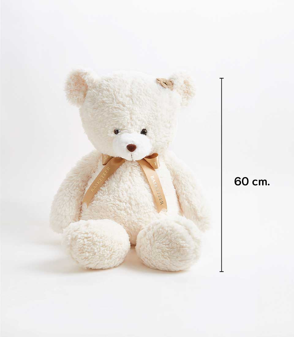 A large fluffy cream teddy bear sits upright with a light brown ribbon around its neck that reads 