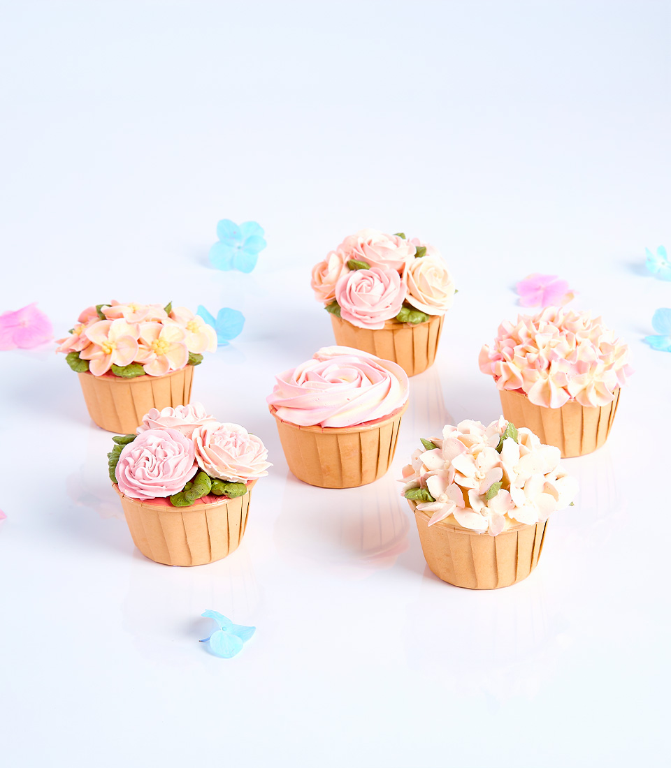 A collection of cupcakes decorated with various floral designs in pink and white frosting.