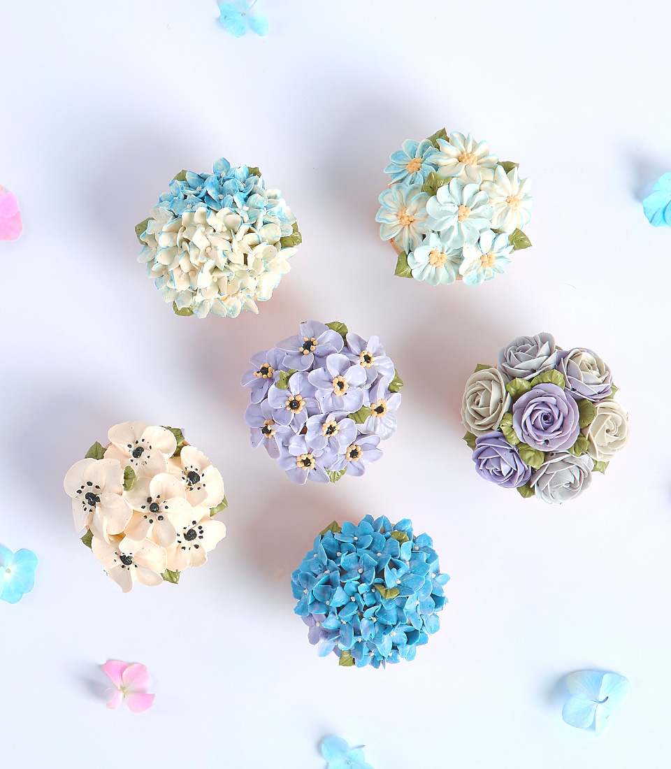Six cupcakes decorated with various floral designs in different colors.
