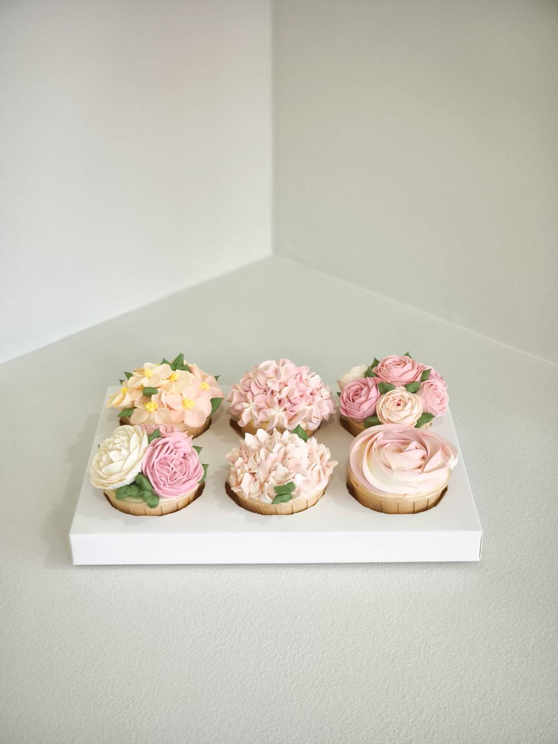 Set of 6 flower-shaped tarts decorated with pastel buttercream flowers including roses, hydrangeas, and camellias in a white box.