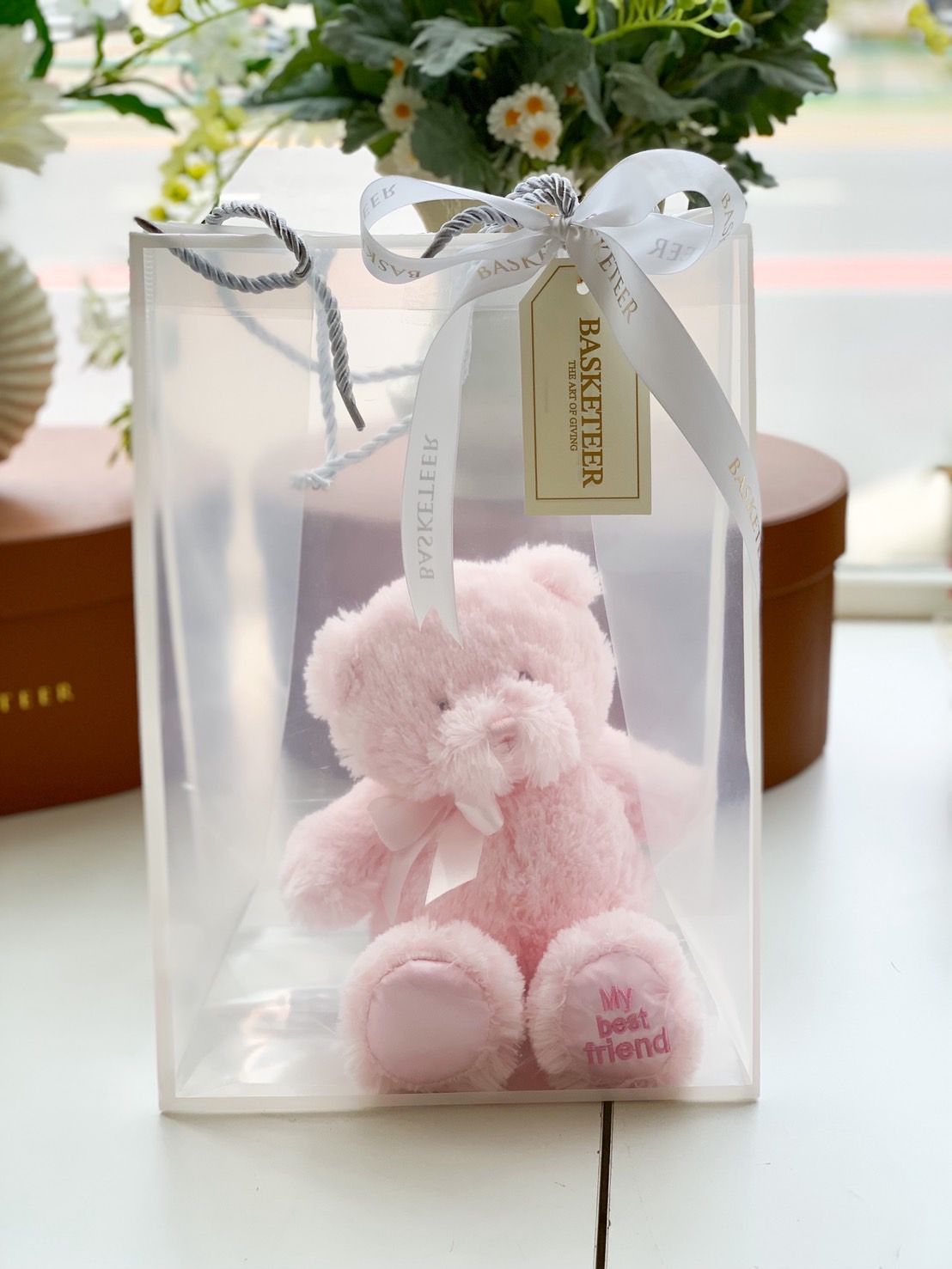 Soft pink teddy bear in a clear gift bag with white ribbon, labelled Basketeer. Cute plush bear with “My best friend” embroidery on foot.