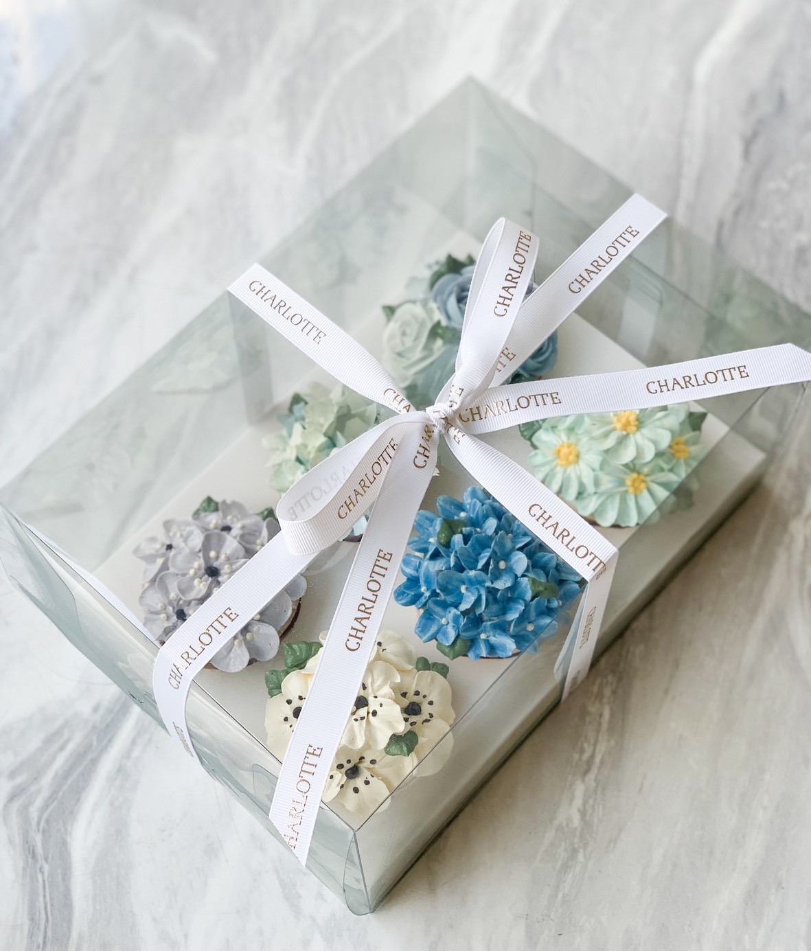 A clear gift box, tied with a white ribbon featuring the name 