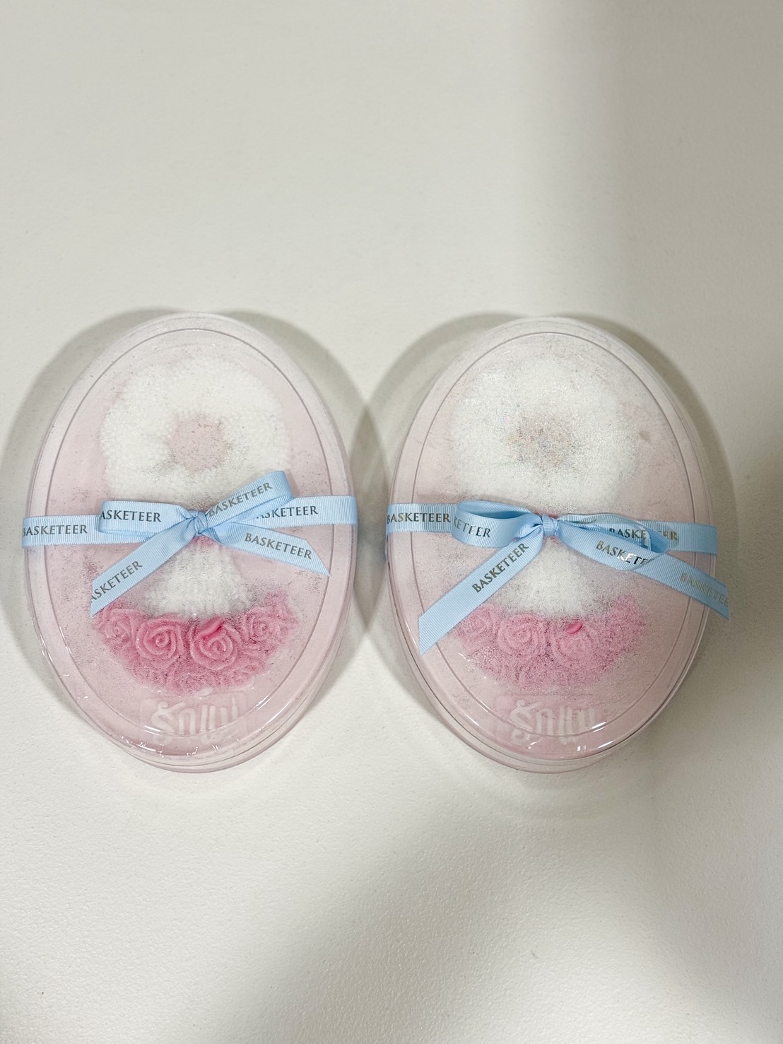 Set of two pink coconut jelly cakes with white jasmine garlands and pink roses, tied with blue “Basketeer” ribbons, “รักแม่” message, Mother’s Day gift.