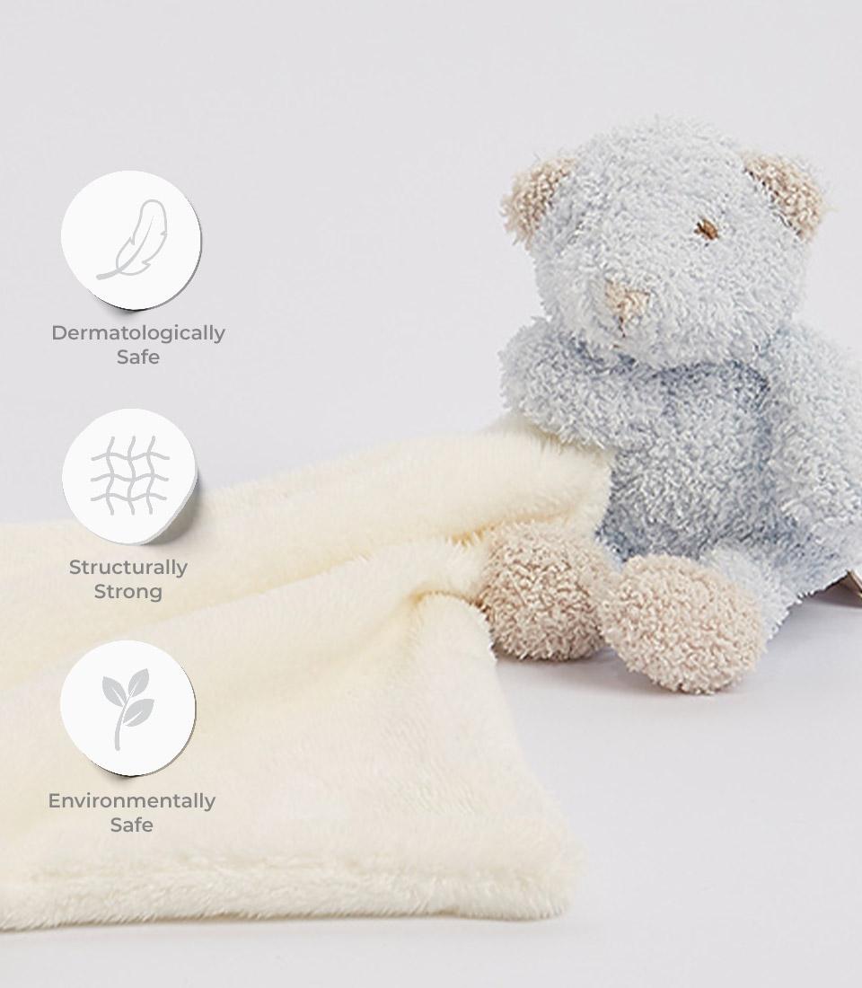 Soft blue teddy bear with a cream-colored comforter, designed for newborns, emphasizing dermatologically safe, structurally strong, and environmentally safe qualities.