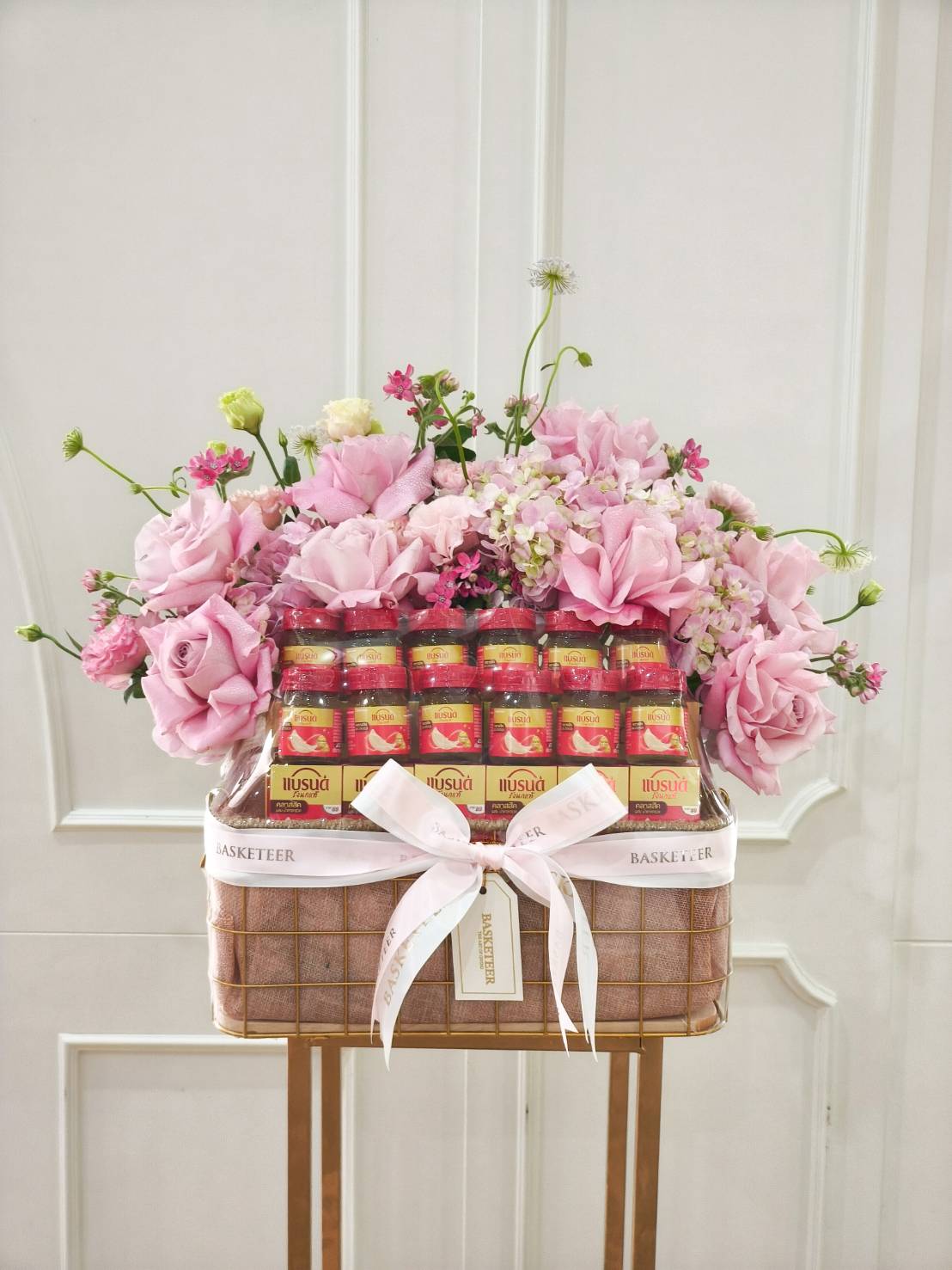 Elegant gift basket filled with Brand’s Bird’s Nest bottles, decorated with pink roses, hydrangeas, and satin ribbon.