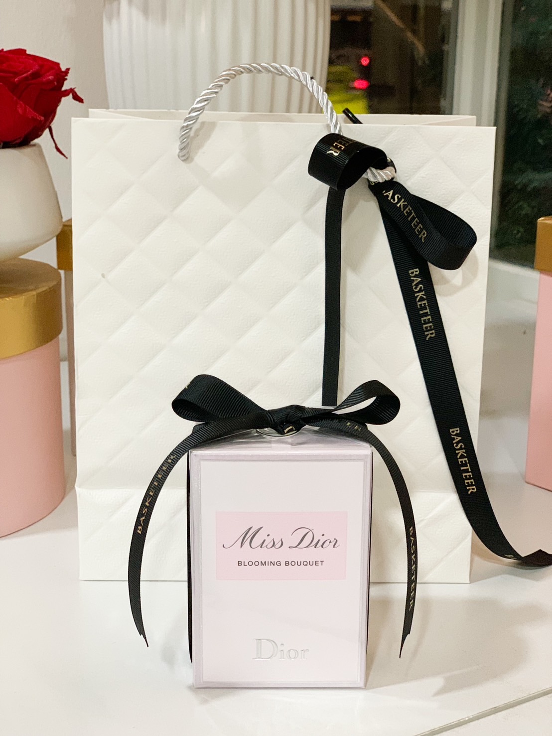 A Miss Dior Blooming Bouquet perfume gift set, elegantly wrapped with a black Basketeer ribbon and paired with a quilted white gift bag.