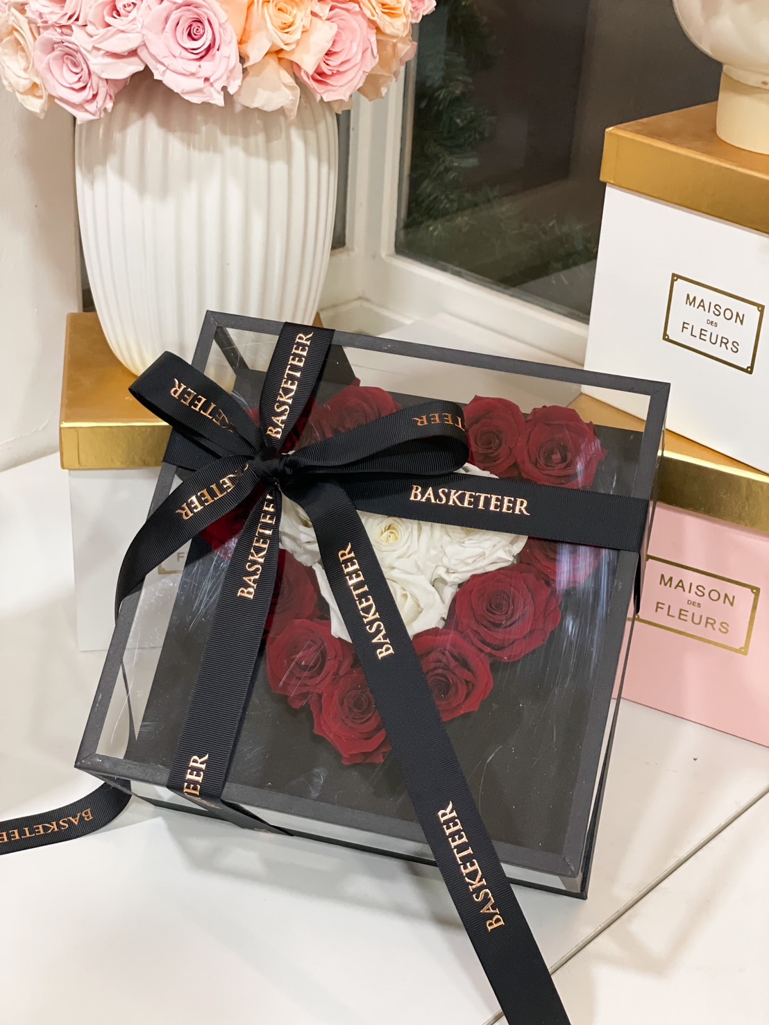 A heart-shaped preserved rose arrangement with red and white roses, elegantly displayed in a black luxury gift box with a satin ribbon.