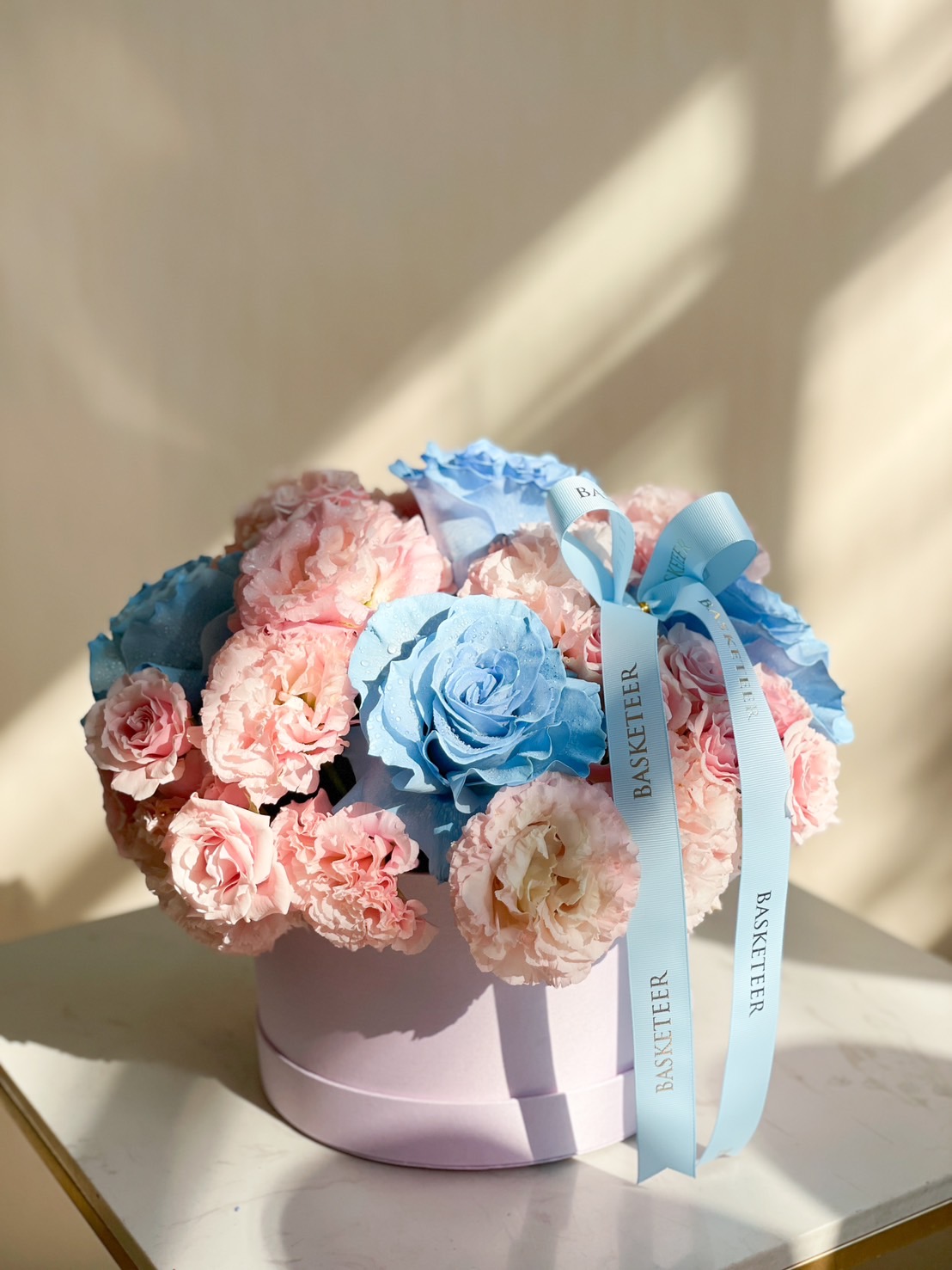 A luxurious flower box with soft blue and blush roses, elegantly arranged with a pastel ribbon, perfect for gifting.
