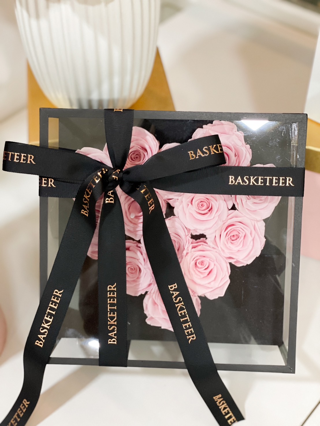A luxurious black glass box filled with soft pink preserved roses, tied with a sophisticated black ribbon, making it a timeless romantic gift.