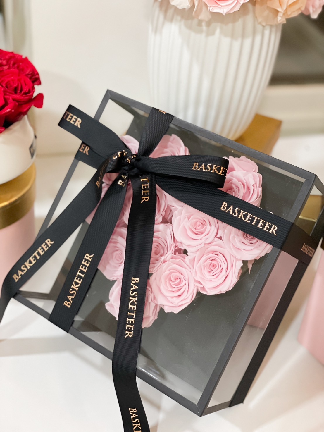A luxurious black glass box filled with soft pink preserved roses, tied with a sophisticated black ribbon, making it a timeless romantic gift.