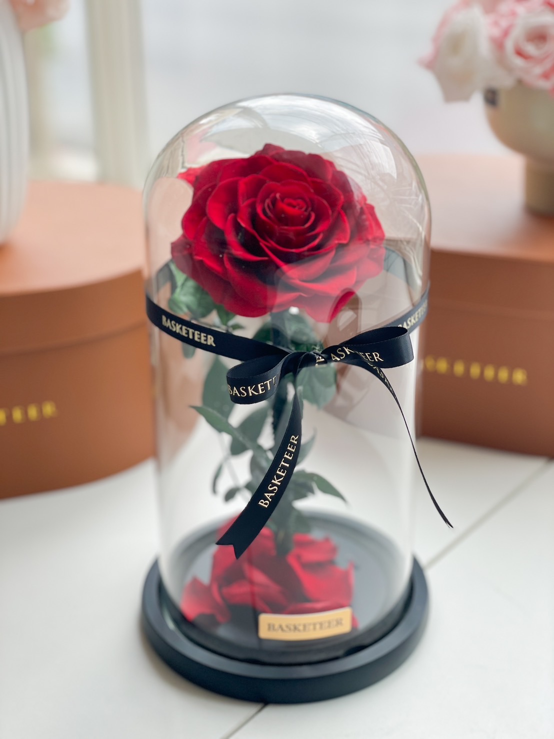 A luxurious preserved red rose encased in a glass dome, set on a black base with scattered petals, perfect for romantic gifting.