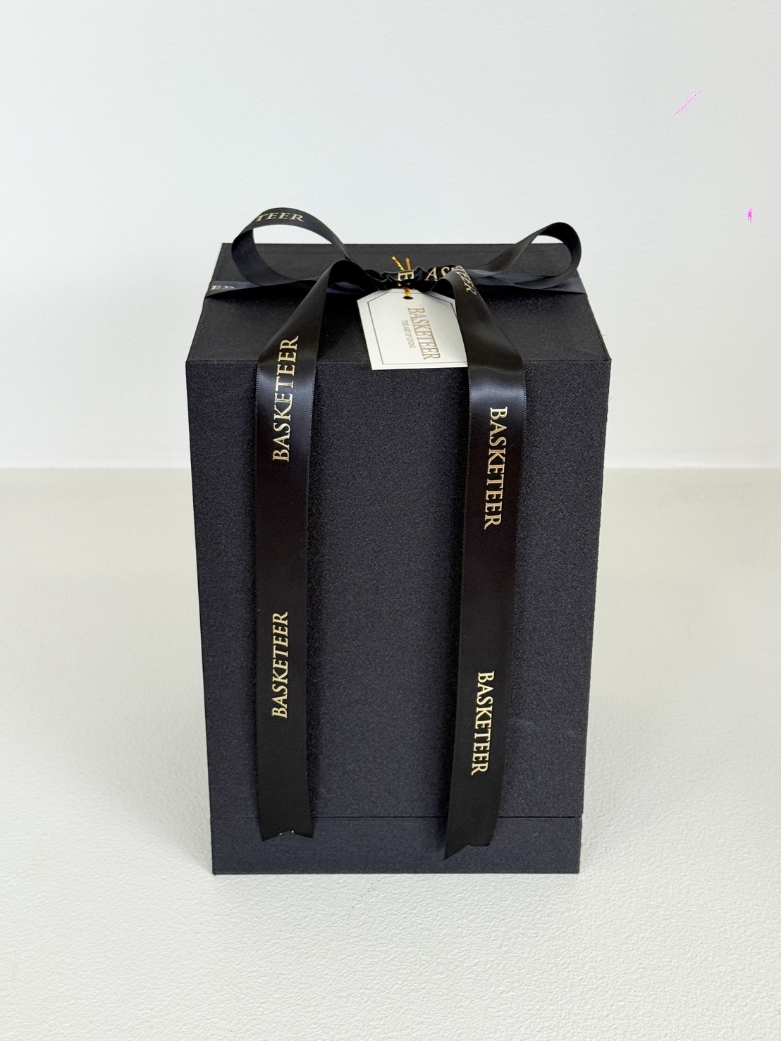 A black gift box with a matching lid, tied with a black ribbon printed with 