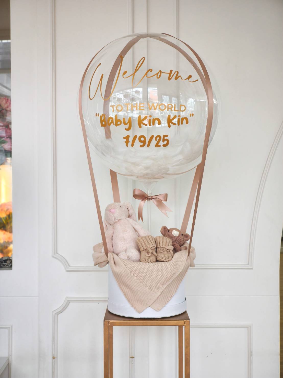 Elegant newborn gift set with transparent balloon, plush toys, baby socks, and beige blanket in a white box.